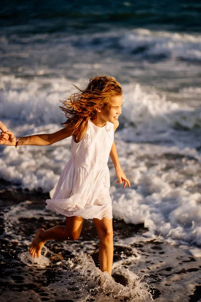 Meisje in witte jurk wandelingen en plezier op zee kust met grote golven en sterke wind. — Stockfoto