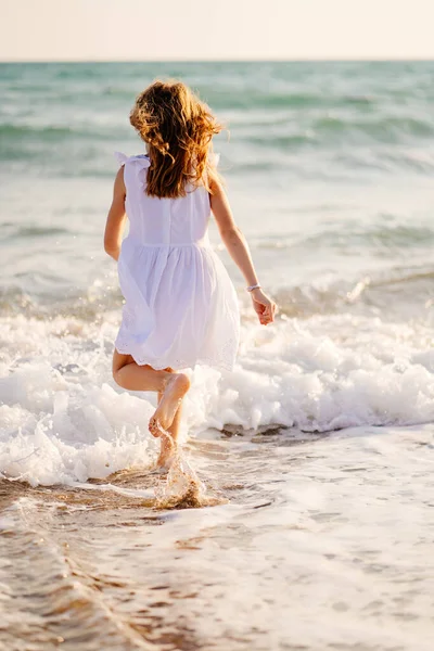 Meisje in witte jurk wandelingen en plezier op zee kust met grote golven en sterke wind. — Stockfoto