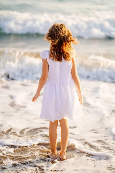 Meisje in witte jurk wandelingen en plezier op zee kust met grote golven en sterke wind. — Stockfoto