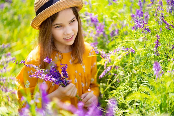 Adolescente chica en sombrero recogiendo un ramo de flores silvestres en un prado . —  Fotos de Stock