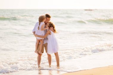 Baba ve kızları rüzgarlı bir havada deniz kıyısında yürüyorlar. eğlenceli aile.