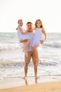 Baba ve kızları rüzgarlı bir havada deniz kıyısında yürüyorlar. eğlenceli aile.