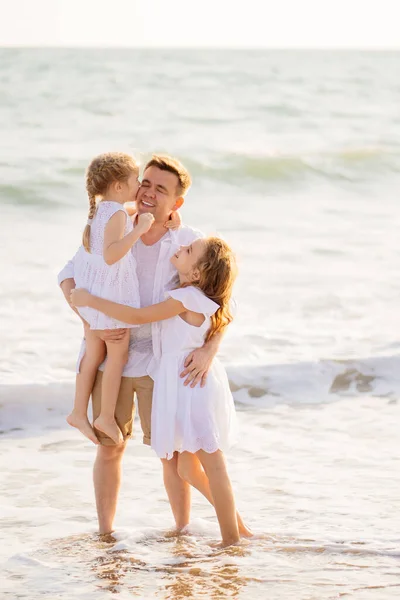 dad with daughters walking along sea-shore in windy weather. fun family.