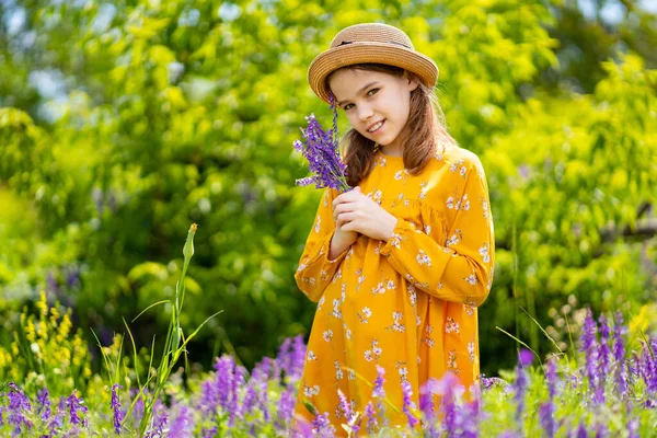 Tiener meisje in hoed plukken een ruiker van wilde bloemen in een weide. — Stockfoto