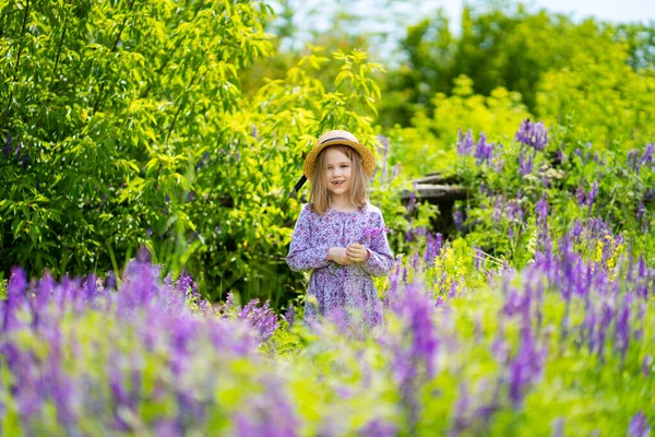 Niña con sombrero recogiendo un ramo de flores silvestres en un prado . — Foto de Stock