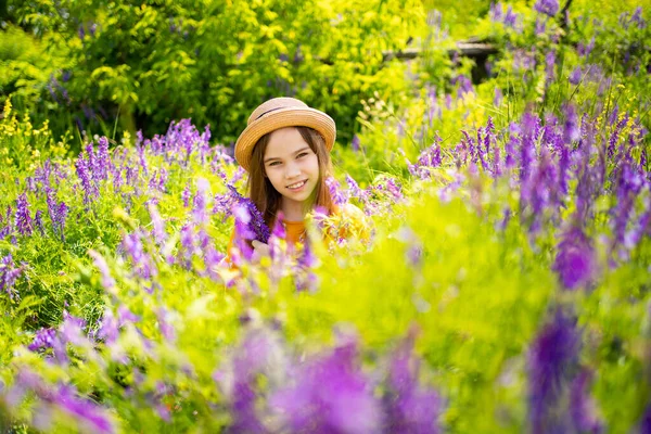 Tiener meisje in hoed plukken een ruiker van wilde bloemen in een weide. — Stockfoto