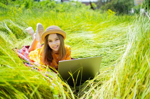 Tonårstjejen lär sig att jobba på laptop på ängen. mobilt Internet på landsbygden. — Stockfoto