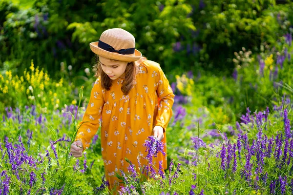 Adolescente chica en sombrero recogiendo un ramo de flores silvestres en un prado . — Foto de Stock