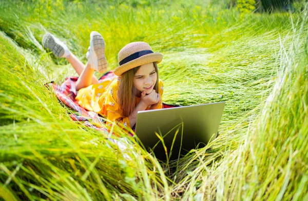 Tonårstjejen lär sig att jobba på laptop på ängen. mobilt Internet på landsbygden. — Stockfoto