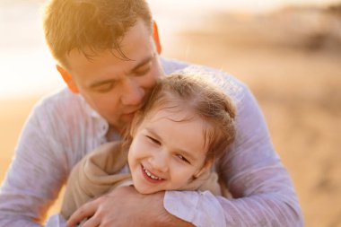 Baba, elbiselerle denizde yüzdükten sonra kızı ısıtır. Islak elbiseli çocuk.