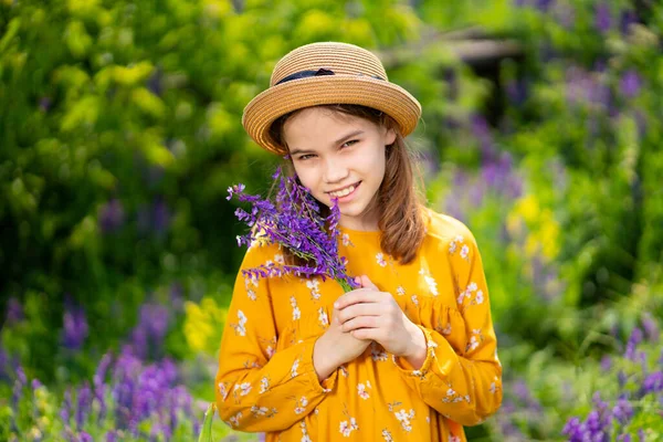 teen girl in hat picking a bouquet of wildflowers in a meadow.