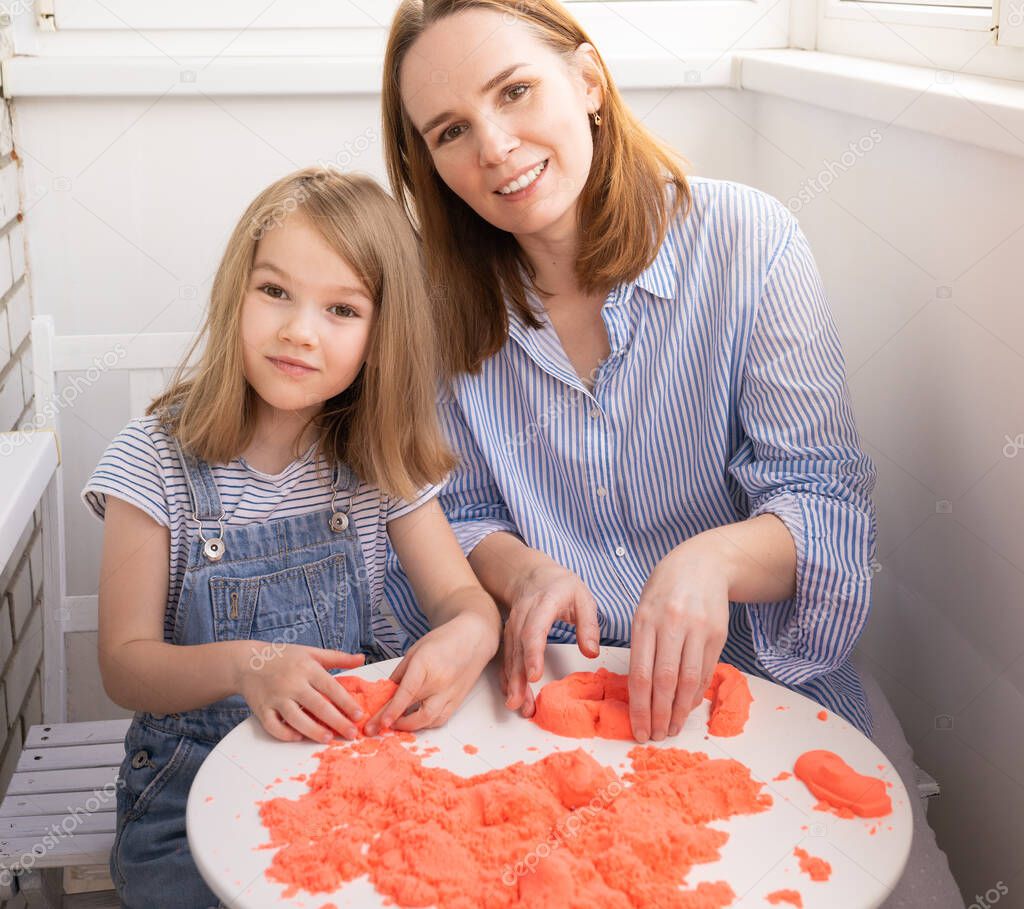 mother and daughter playing with kinetic sand. development of fine motor skills.