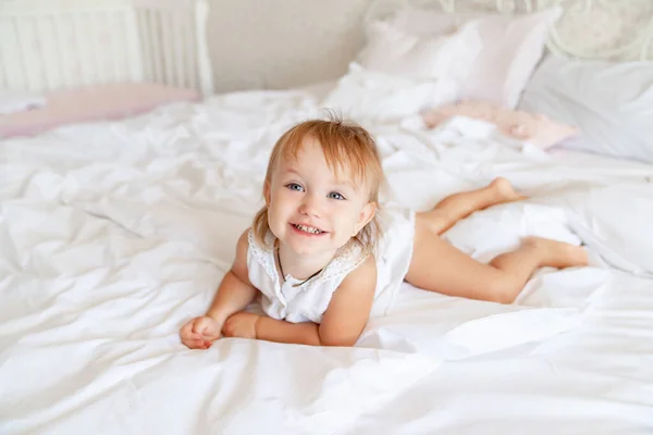 Niña en la cama en el dormitorio y se ríe. feliz infancia . — Foto de Stock