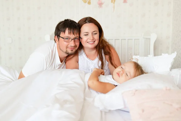 Los padres miran a la niña dormir en la cama en el dormitorio con coronas. — Foto de Stock