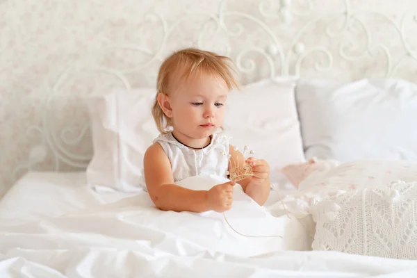 Niña sentada en la cama en el dormitorio con corona. Fiesta de cumpleaños princesa . — Foto de Stock