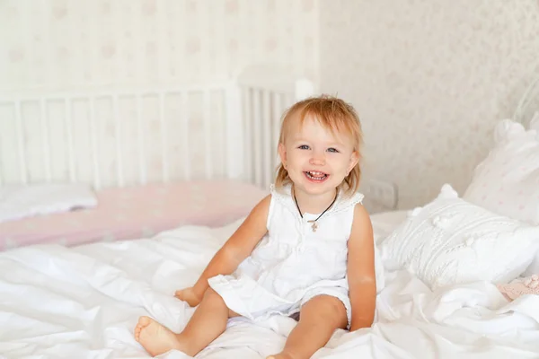 Niña en la cama en el dormitorio y se ríe. feliz infancia . — Foto de Stock