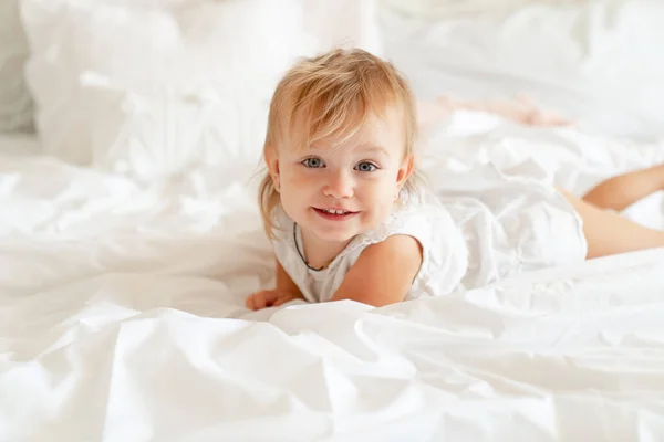 Niña en la cama en el dormitorio y se ríe. feliz infancia . — Foto de Stock