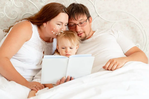 Parents reading book to daughter in bed. place for text on white paper. — Stock Photo, Image