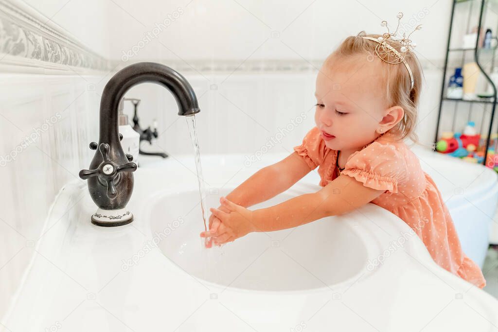 baby girl in crown, washes hands in bathroom. hygiene and cleanliness. 