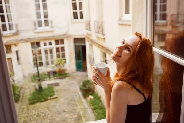 Donna che beve caffè al mattino dalla finestra con vista sul cortile interno . — Foto Stock