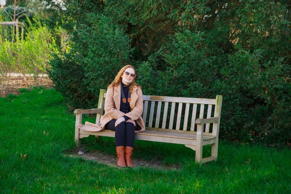 Chica con abrigo sentada en el banco en Spring Park. camina al aire libre . — Foto de Stock