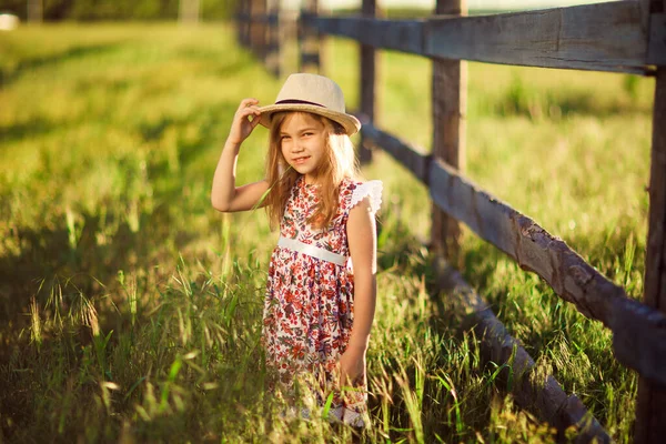Child, girl in hat standing next to fence in village. walks in countryside. — Stock Photo, Image