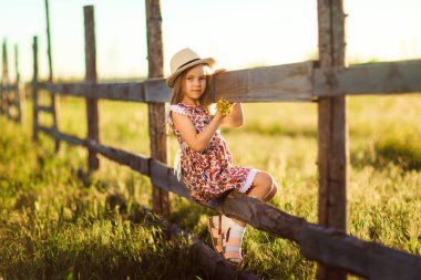 Çocuk, şapkalı kız köyde çitin üstünde oturuyor. Kırsalda yürür.