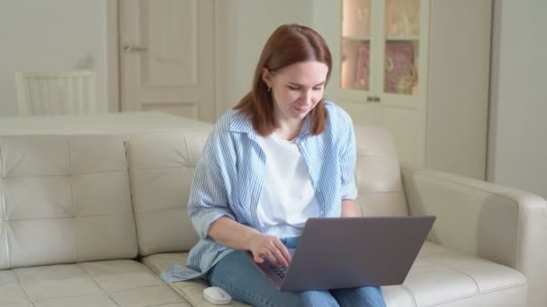 Mujer usando el ordenador portátil, escribiendo texto, sentado en el sofá. enfermo y tos — Vídeos de Stock