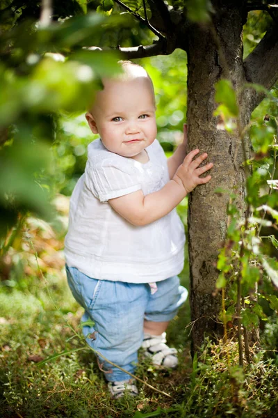 Liten flicka sitter på gräs i trädgården under små äppelträd. Trädgårdsodling. — Stockfoto