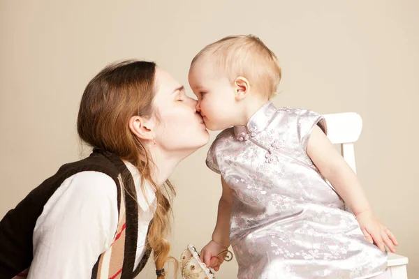 Mutter küsst kleines Mädchen mit kurzen Haaren im Kleid mit kleinem Spielzeugschirm — Stockfoto