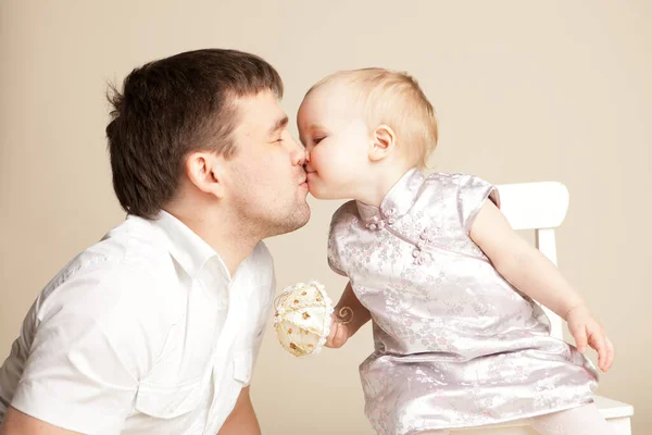 Papá besa niña pequeña con pelo corto en vestido con paraguas de juguete pequeño — Foto de Stock