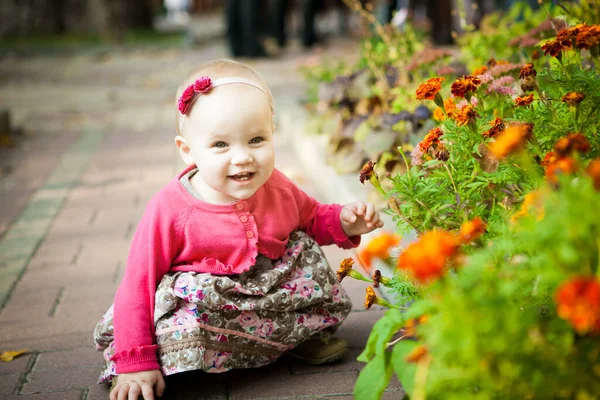 Kleines Mädchen im Kleid sitzt auf der Straße in der Nähe von Blumenbeeten. Spaziergänge im Freien. — Stockfoto