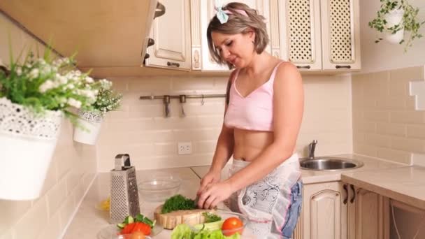 Sexy blondynka gospodyni z tatuaże tnie zielenie dla sałatka w kuchnia. — Wideo stockowe