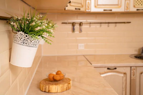 Tazón de huevos hervidos en soporte de madera en la mesa en la cocina brillante, flores en la pared . — Foto de Stock