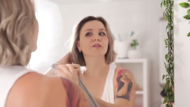 Сексуальная девушка с татуировками делает уборку, стирает зеркало дома — стоковое видео