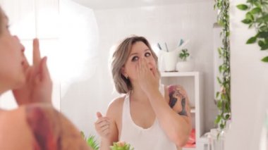 Dövmeli seksi kız aynaya bakar, yüzüne krem sürer ve saçlarını yaptırır..