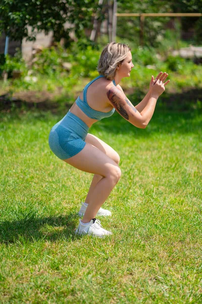 Boční pohled.squat cvičení. dívka hraje sport na zahradě. fitness po porodu — Stock fotografie