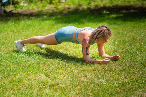 Cvičební prkno, stojan. blondýny dívka s tetováním hraje sport v zahradě. — Stock fotografie