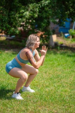 Yan görüş. Çömelme egzersizleri. Kız bahçede spor yapıyor. doğumdan sonra fitness