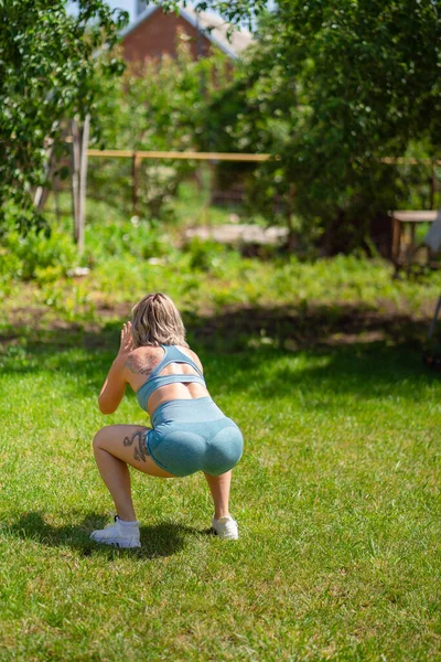 squat, jumping exercises. girl plays sports in garden. fitness after childbirth.