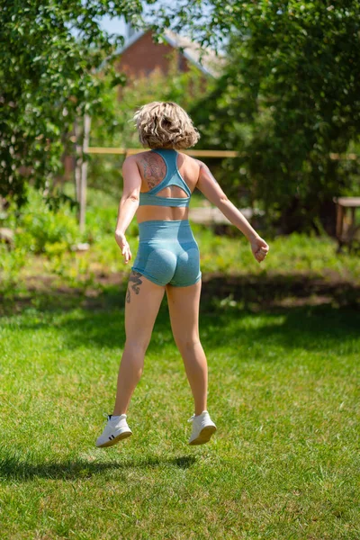 Squat, des exercices de saut. fille fait du sport dans le jardin. forme physique après l'accouchement. — Photo
