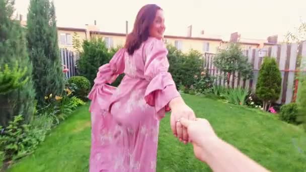 Happy brunette woman in dress dancing and spinning in garden, being led by hand. — Stock Video