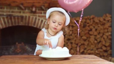 Beyaz elbiseli ve şapkalı küçük kız, şenlikli elleriyle pasta yiyor..