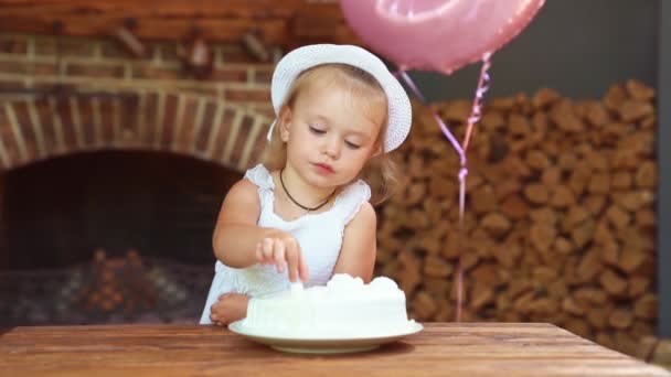 Petite fille en robe blanche et chapeau, manger festif avec son gâteau mains. — Video
