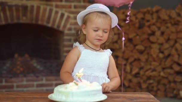 Menina criança em vestido branco e chapéu soprando vela, número três no bolo . — Vídeo de Stock