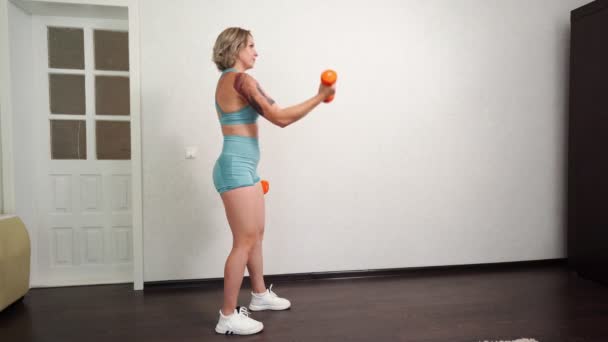 Mädchen mit Tätowierungen treibt zu Hause Sport und macht Übungen mit Hanteln. — Stockvideo