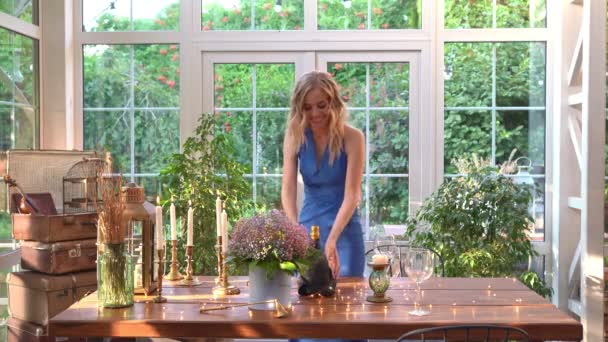 Chica en vestido azul establece mesa, guirnalda, vino y copas. cena romántica . — Vídeos de Stock