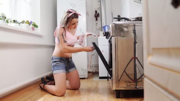 Blond i shorts och med tatueringar kock i kök i ugn. — Stockvideo