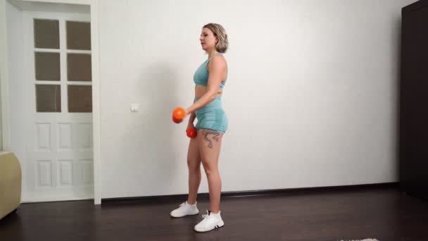 Женщина с татуировками занимается спортом дома, делая упражнения с гантелями . — стоковое видео