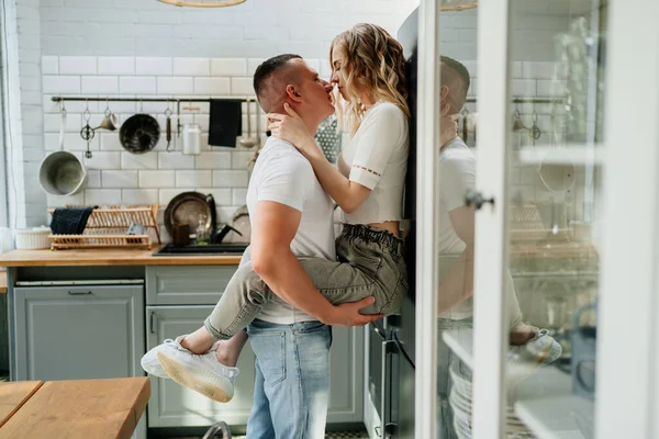 Пара влюбленных целуются и обнимаются на кухне рядом с холодильником. — стоковое фото
